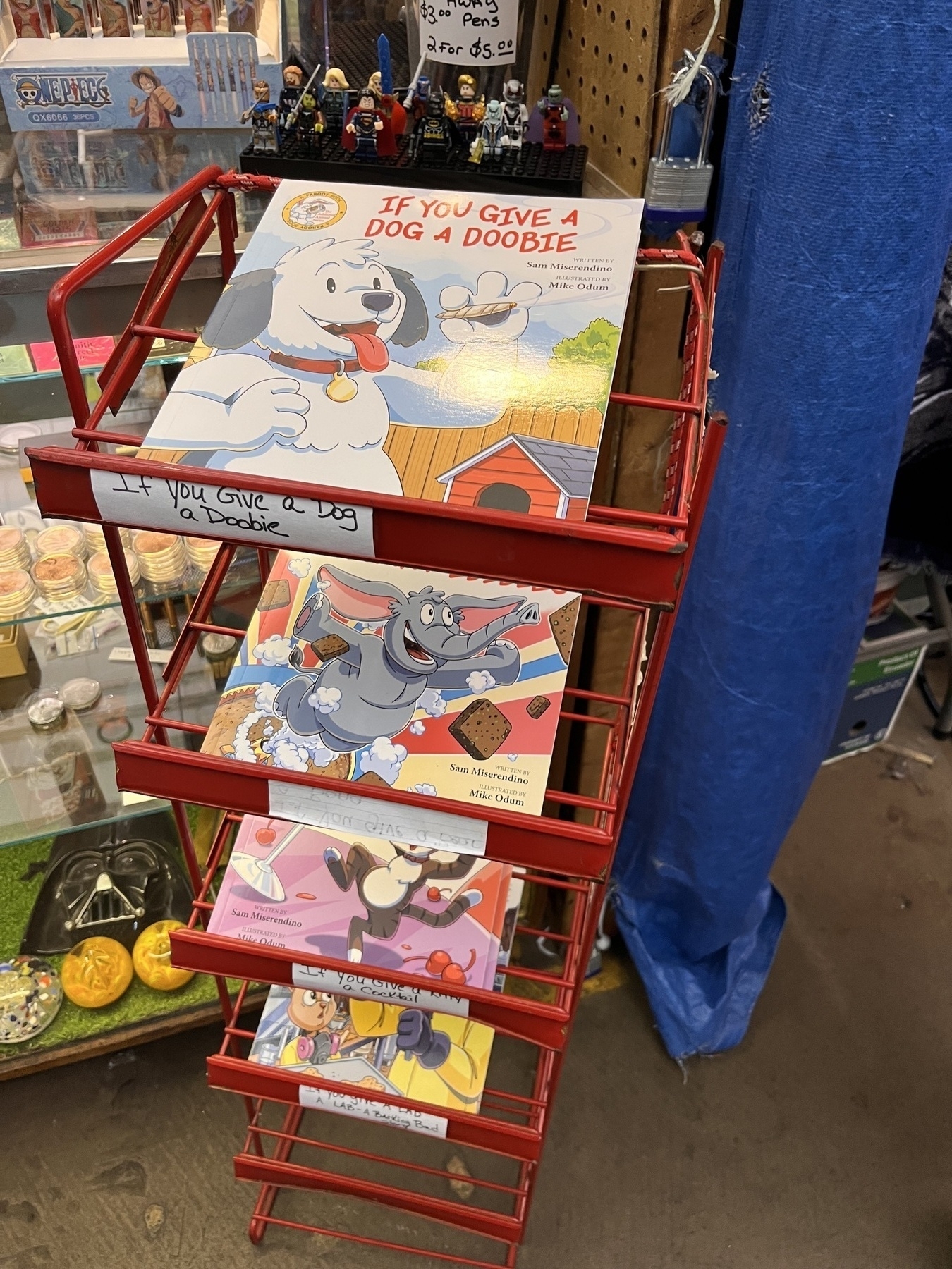 A rack of magazines, the top one being a children’s book called “If you give a dog a doobie”. It pictures a cartoon dog holding a joint. 