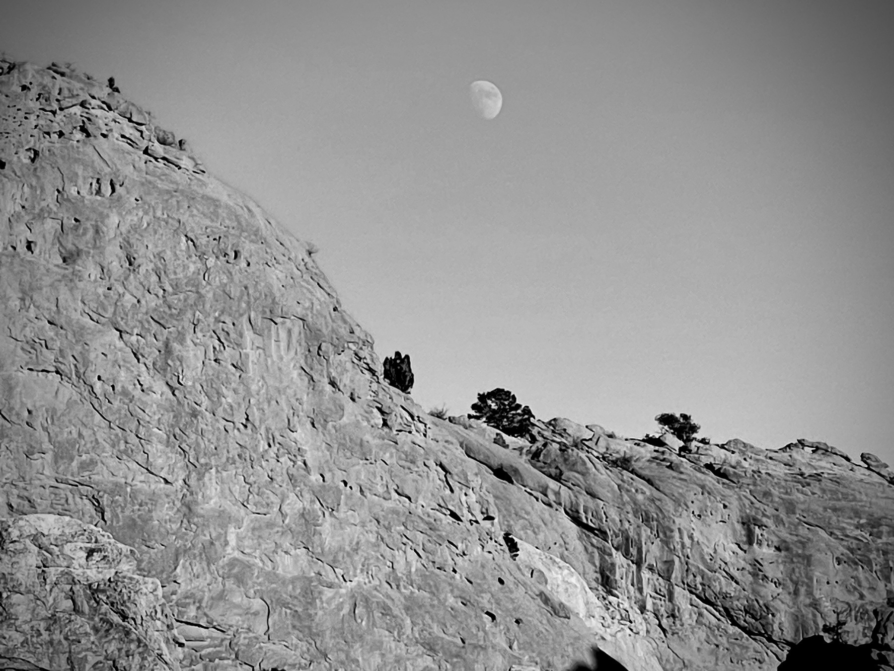 Black and white photo of a rocky cliff with a pale moon in the daytime sky