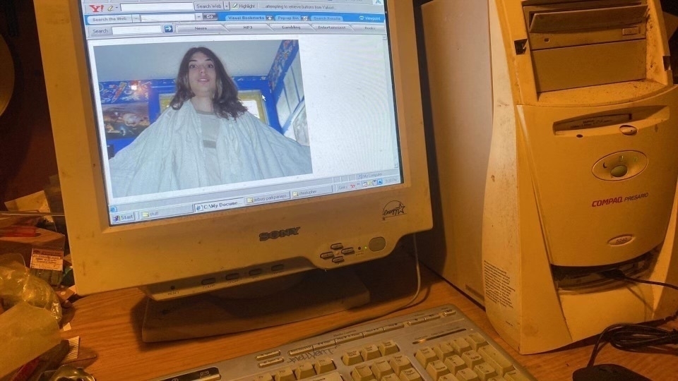 A old company tower computer with a Sony crt monitor showing an ancient version of windows. A photo of yours truly, a white man, is on display. I’m about 17 years old, clean shaven, with long flowing brown hair. I’m spreading my arms with wide eyes staring into camera. 