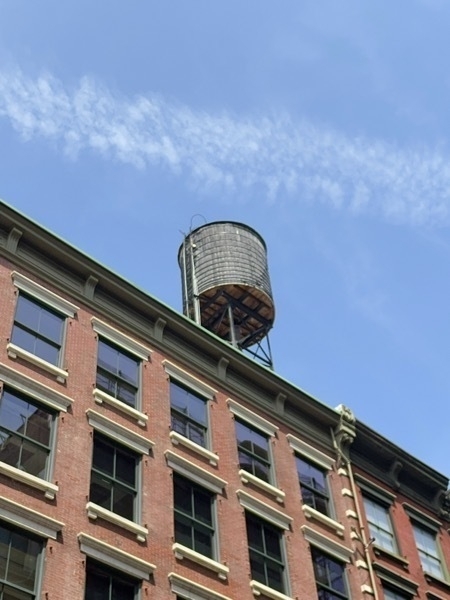 A low angle shot of a water tower on top of a brownstone building over a bright blue sky shot with thin clouds