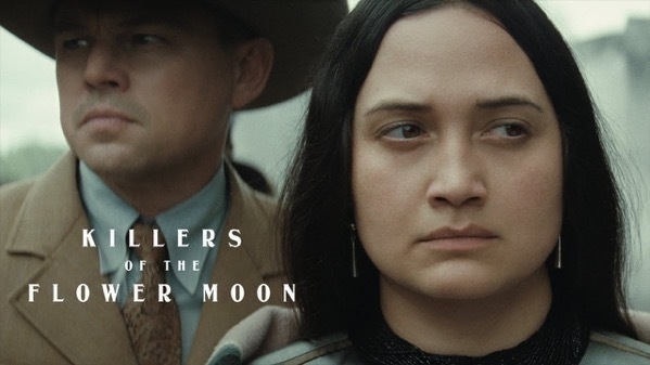 A screen grab from the movie killers of a flower moon. Tight two shot cropping just the heads. In the foreground, a native american woman, played by Lily Gladstone, looking worried off to the right. Behind her, a white man in a cowboy hat and tie, played by Leonardo DiCaprio, looks off blankly