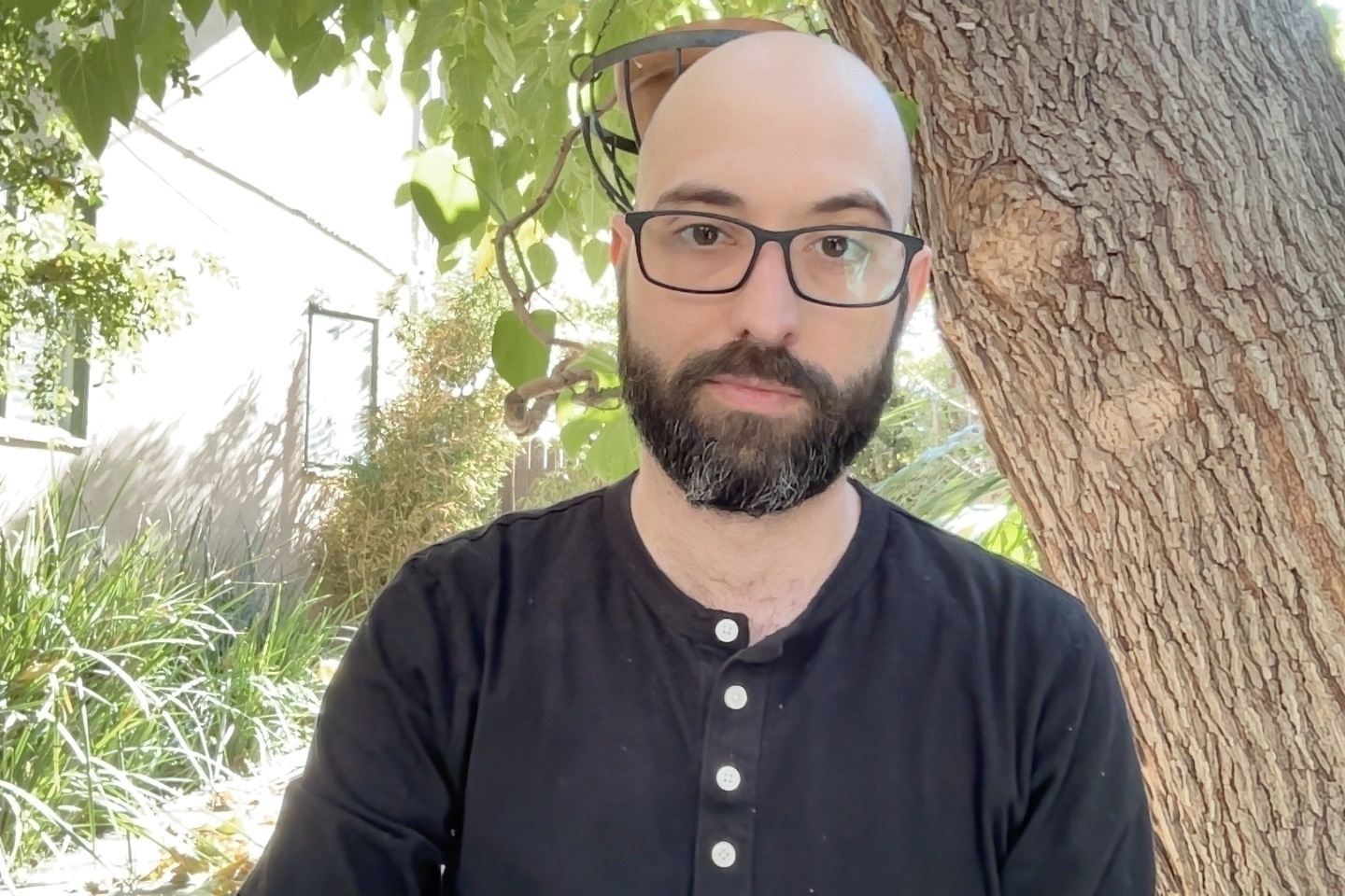 A photo of me, a bald, bearded white man. I’m sitting outside near a tree, sun speckles lighting everything up. My expression is almost blank, with a weird-ass hint of a smile. I’m creeped out of myself in retrospect.