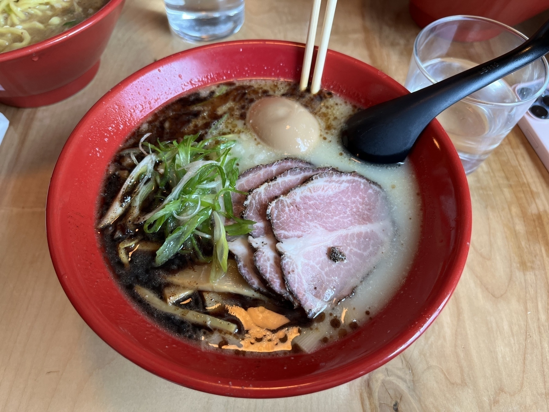 A bowl of ramen with garlic oil on the side, pork slices, a soy sauce egg, chives. 