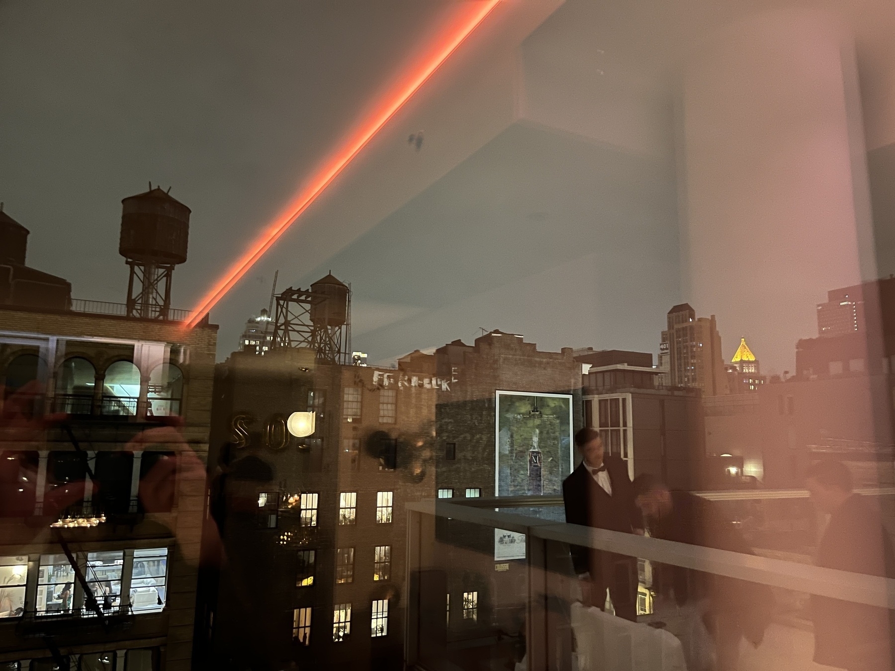 New York City skyline through a full screen window, the reflection of a red line in it seeming to shoot from a water tower in silhouette 
