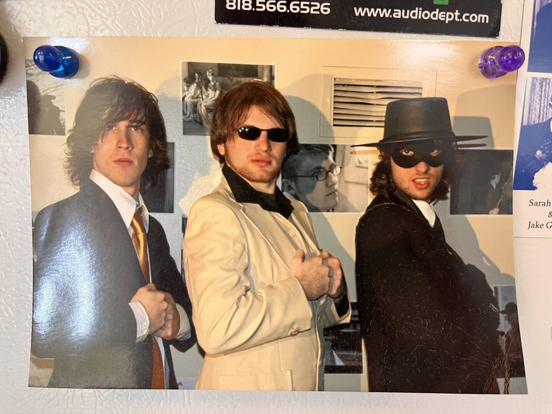 Three young white men wearing suits and serious expressions. Me, on the right, is wearing an eye mask and hat and a sneer. 