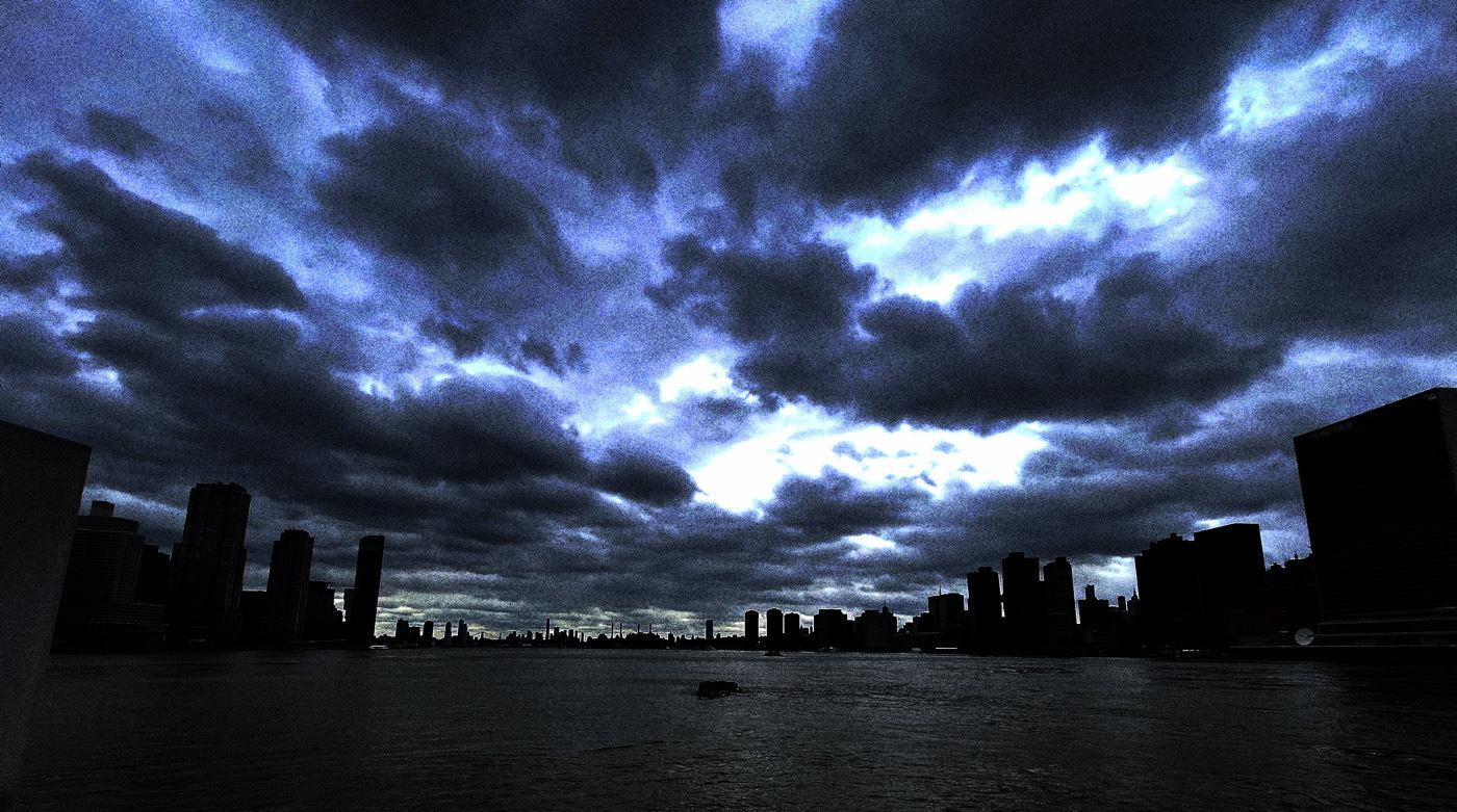 A majestic city skyline stands against a turbulent sky. Dark, ominous clouds loom over the silhouetted buildings, casting an eerie glow reflected in the calm waters below. The contrast between the dark clouds and the cityscape evokes a sense of awe and mystery. 🌆🌧️