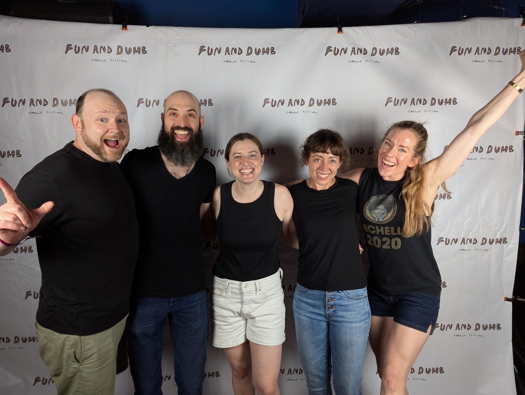 Five people smiling and posing in front of a fun and dumb branded background.
