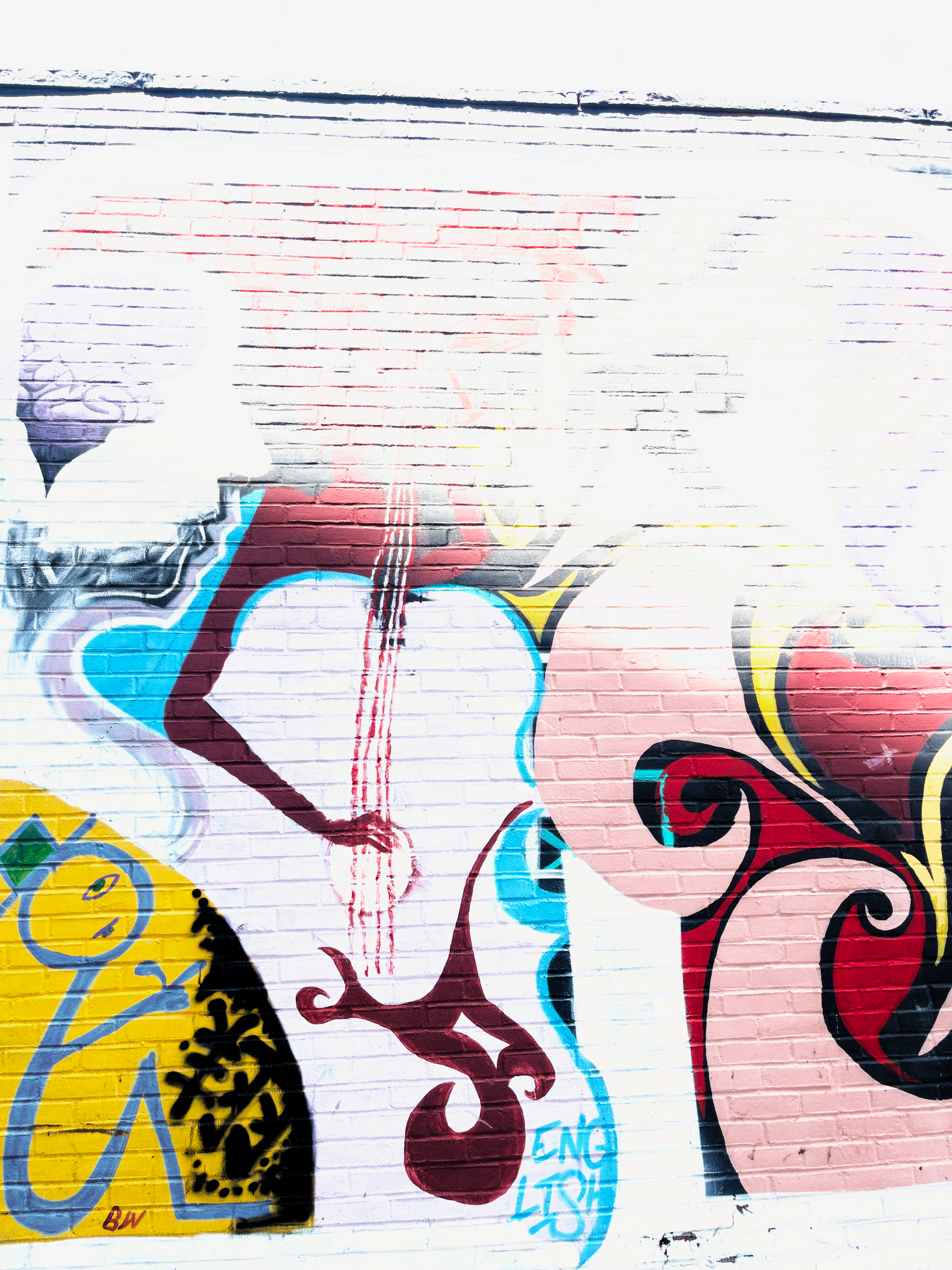 Auto-generated description: A colorful graffiti mural features abstract shapes, swirling patterns, and a cartoonish figure on a brick wall.