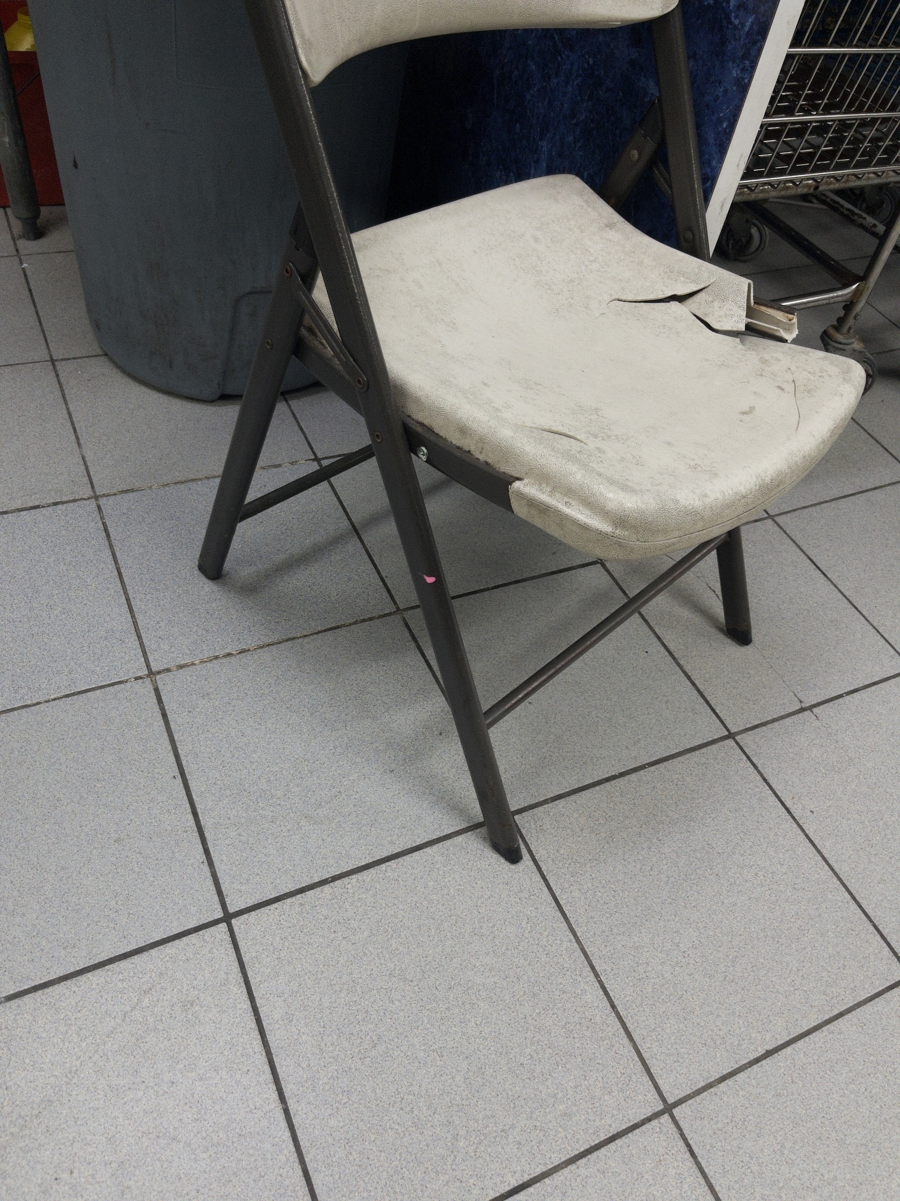 A beat up plastic chair that’s broken on one side. There’s a shadow of the legs and seat below it.