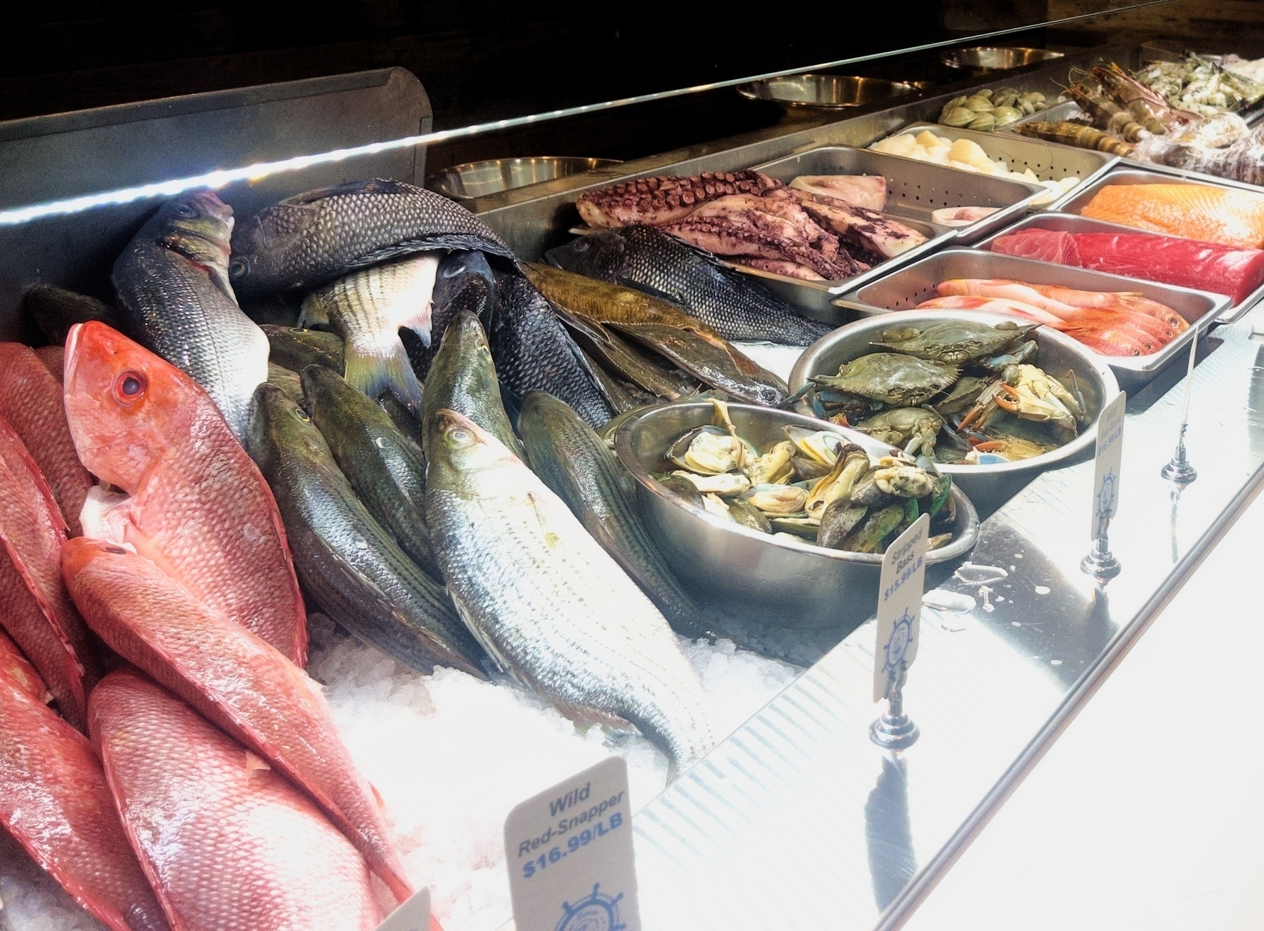 Auto-generated description: A display of fresh seafood, including various fish, shellfish, and octopus, arranged on ice in a market setting.