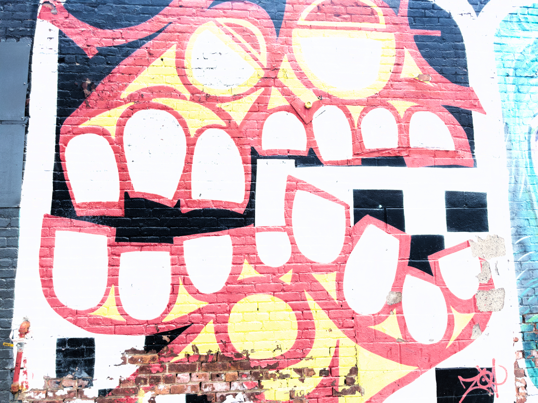 Auto-generated description: A vibrant mural on a brick wall features stylized red and yellow teeth with geometric shapes.