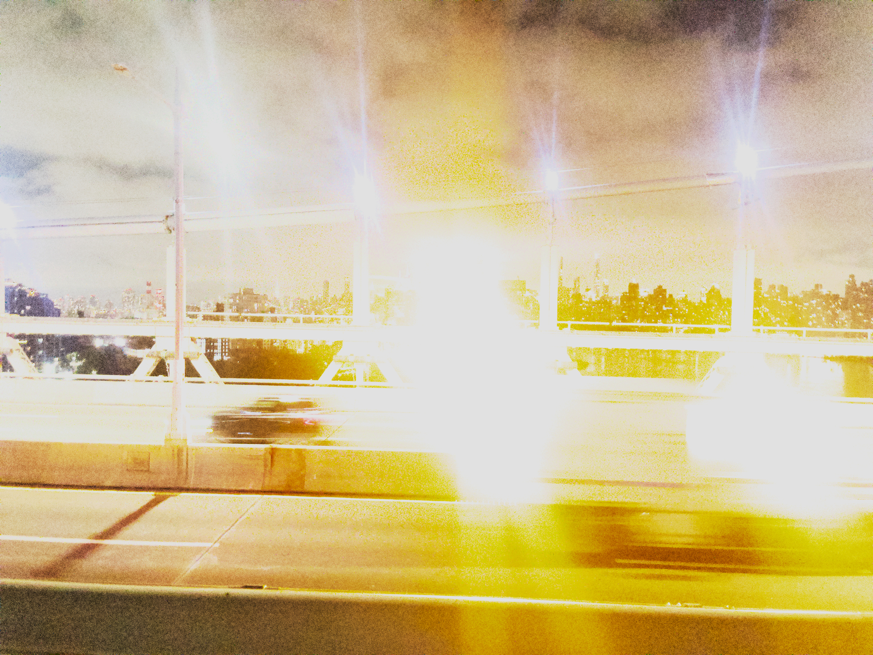 Auto-generated description: A brightly lit city skyline is visible in the background, with blurred car lights streaking across a bridge in the foreground.