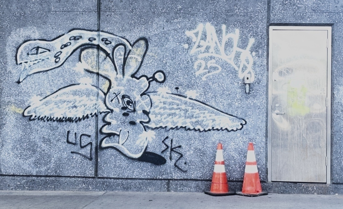 Auto-generated description: A graffiti mural featuring an abstract creature with wings is painted on a wall next to a metal door with two orange traffic cones in front.